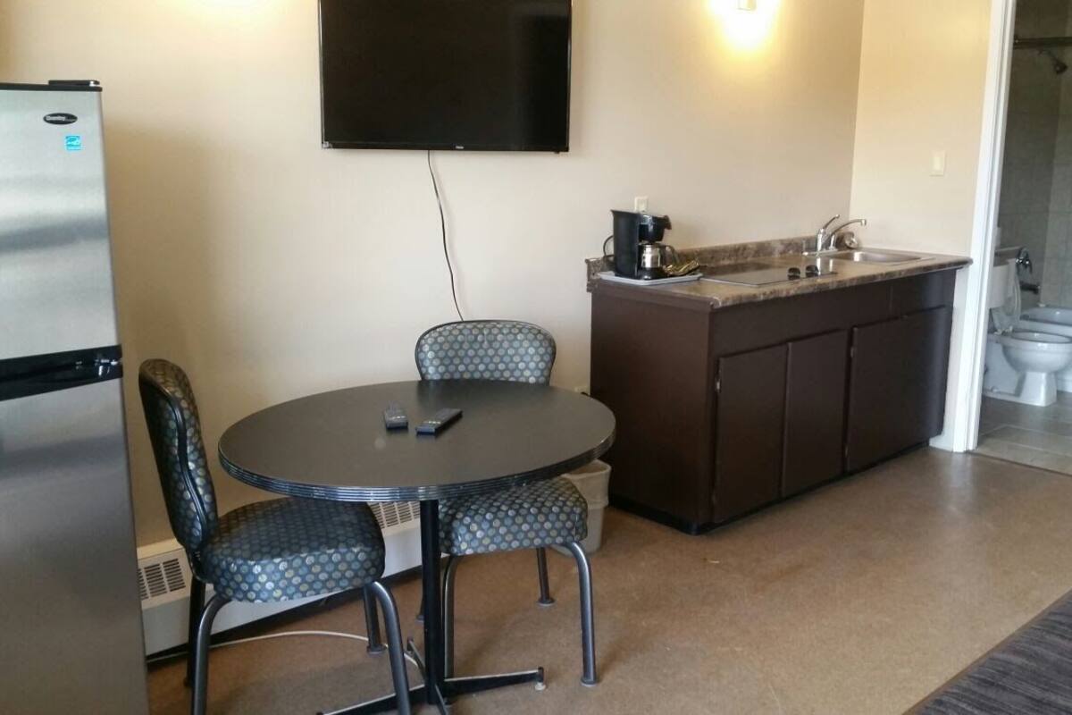 A compact kitchen with a dining table and chairs, a refrigerator, a coffee maker, and a sink.