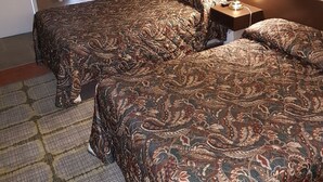 Una camera d'albergo con due letti, un comodino con una lampada, una porta e una finestra con tende.