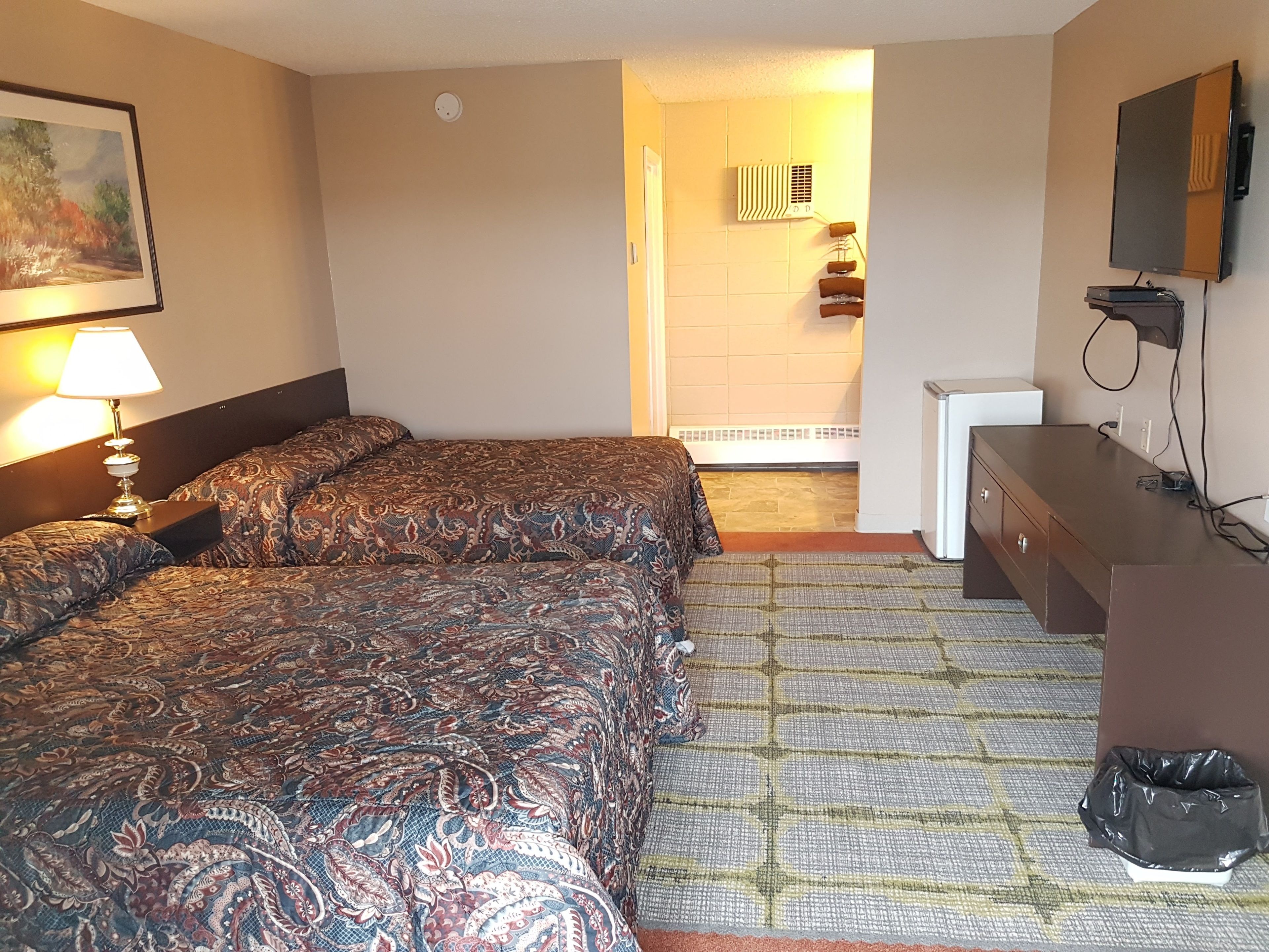 A hotel room with a bed, a desk, a TV, and a painting on the wall.
