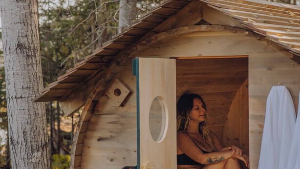 Una cabaña de madera con una puerta circular, una ventana pequeña y una toalla colgada en la pared.