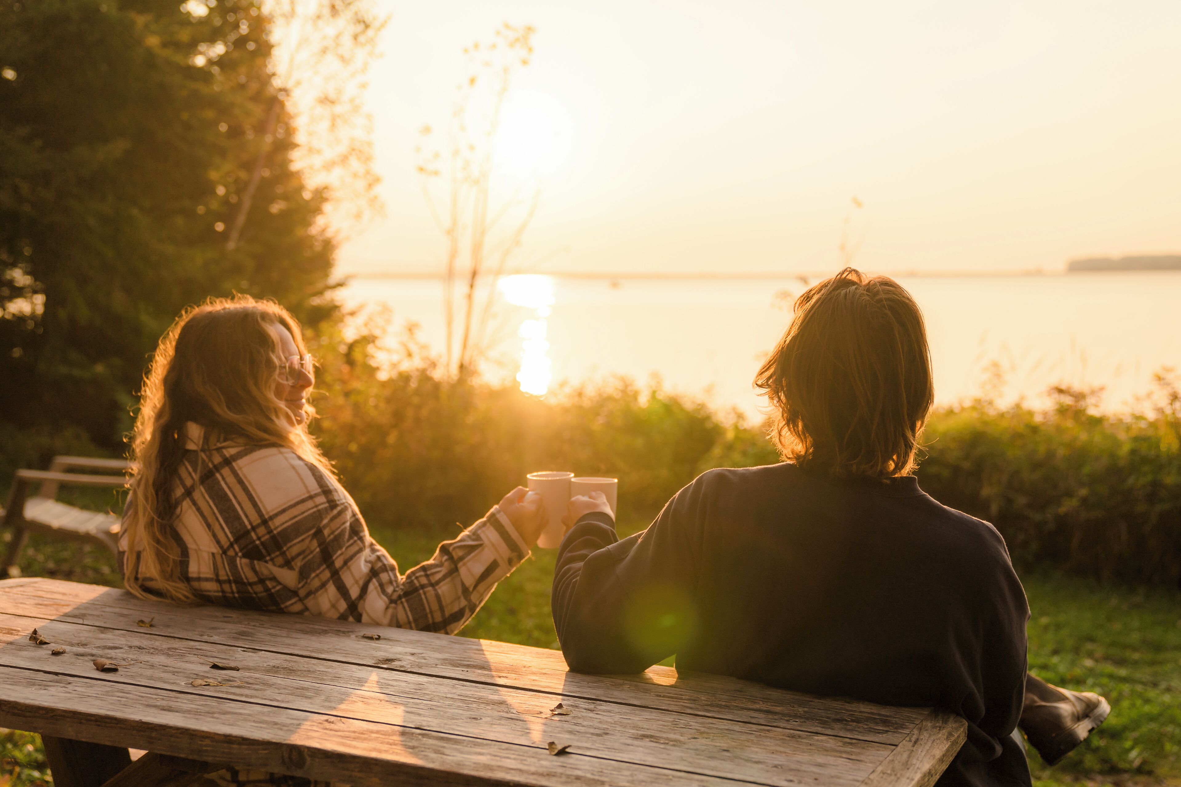 Zwei Personen sitzen bei Sonnenuntergang an einem Holztisch draußen.