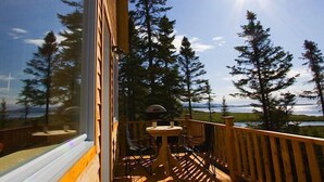 Una terraza de madera con una mesa y sillas, con vistas a un lago y zona boscosa.
