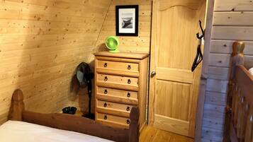 A wooden room with a bed, a dresser, a door, and a framed picture on the wall.