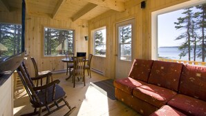 Una cabaña de madera con comedor, sofá y ventanas amplias que dan vistas al bosque y al agua.