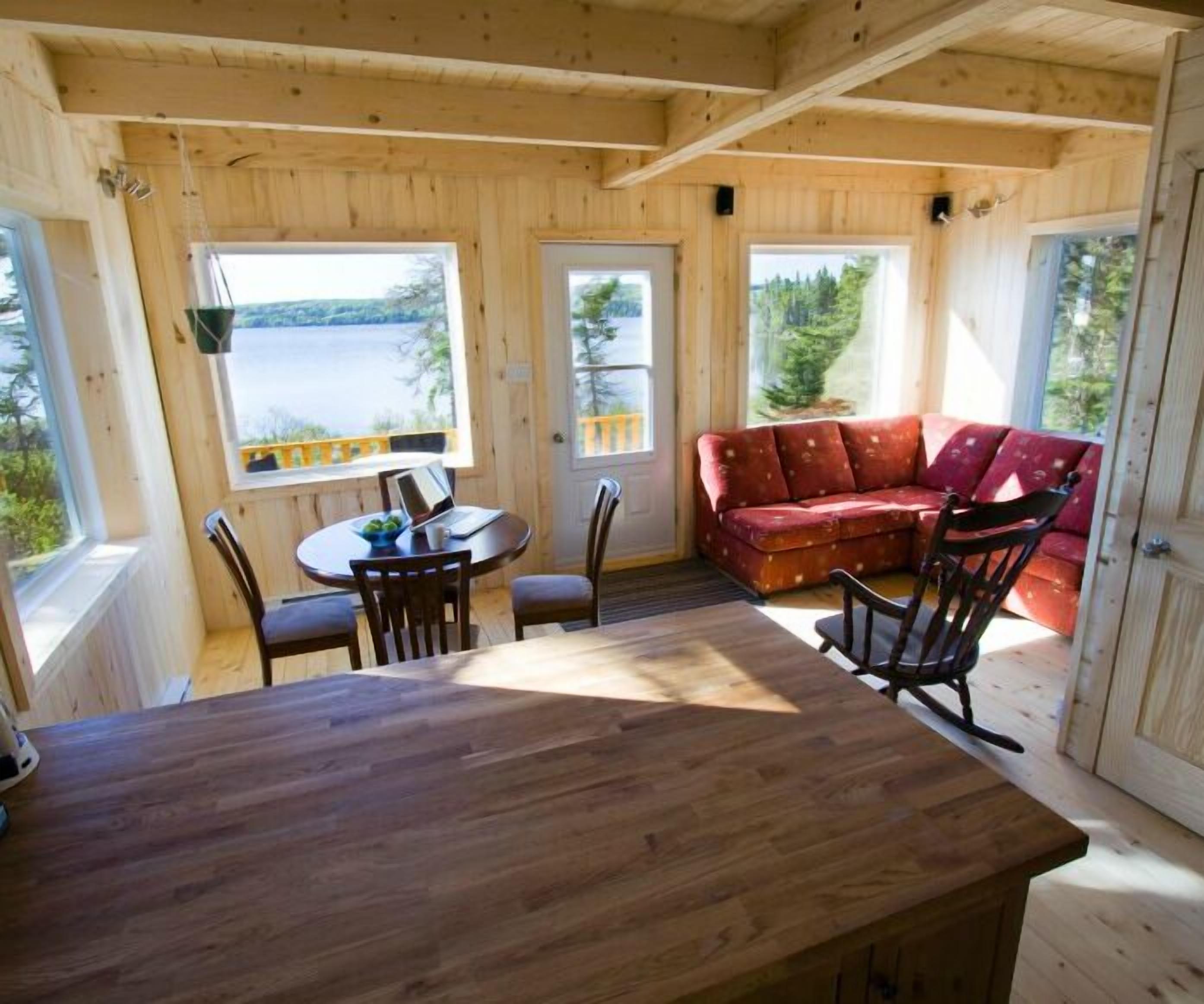A wooden cabin with a dining table, chairs, and a red sofa.