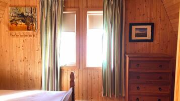 A wooden room with a bed, a dresser, and two windows with curtains.