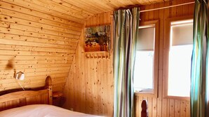 Un dormitorio de cabaña de madera con una cama, una ventana con cortinas y una lámpara de pared.