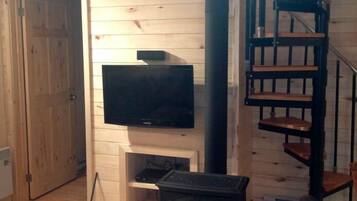 Ett rum med träpanel på väggarna, en öppen spis, en tv som hänger ovanför spisen och en spiraltrappa.