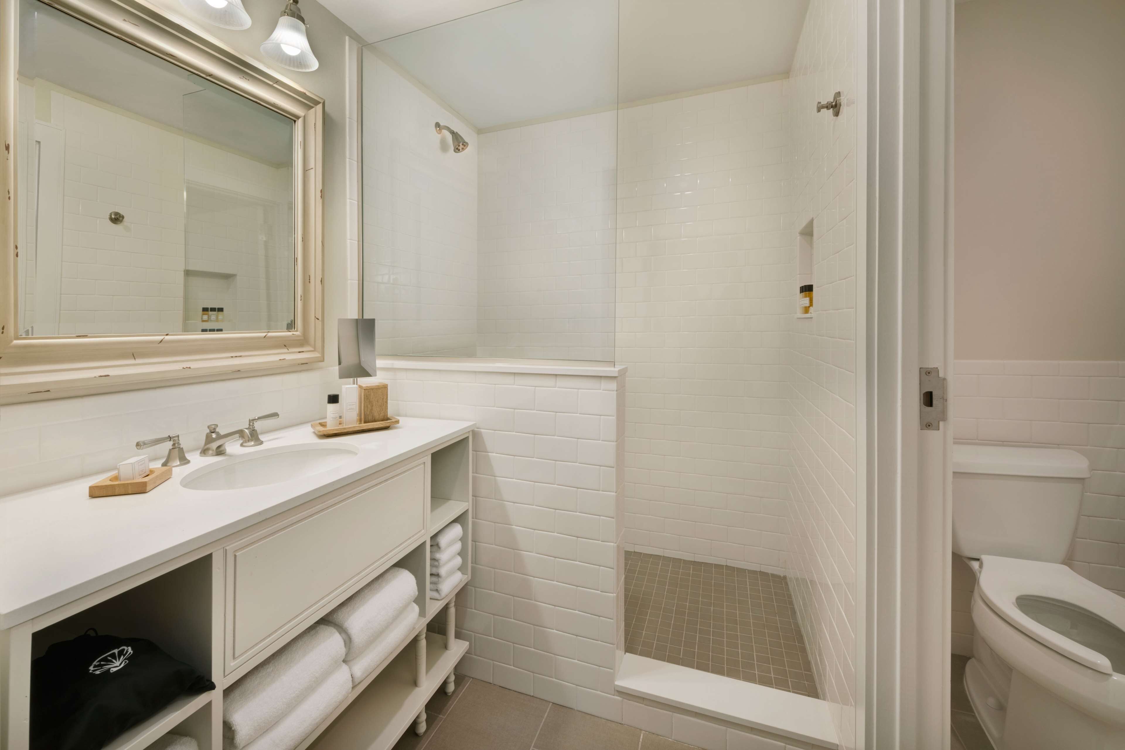 A modern bathroom with a large mirror, two sinks, a shower, and a toilet.