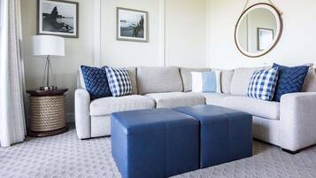 Un salón con un sofá gris, almohadas azules y blancas a cuadros, un espejo redondo y un reposapiés azul.