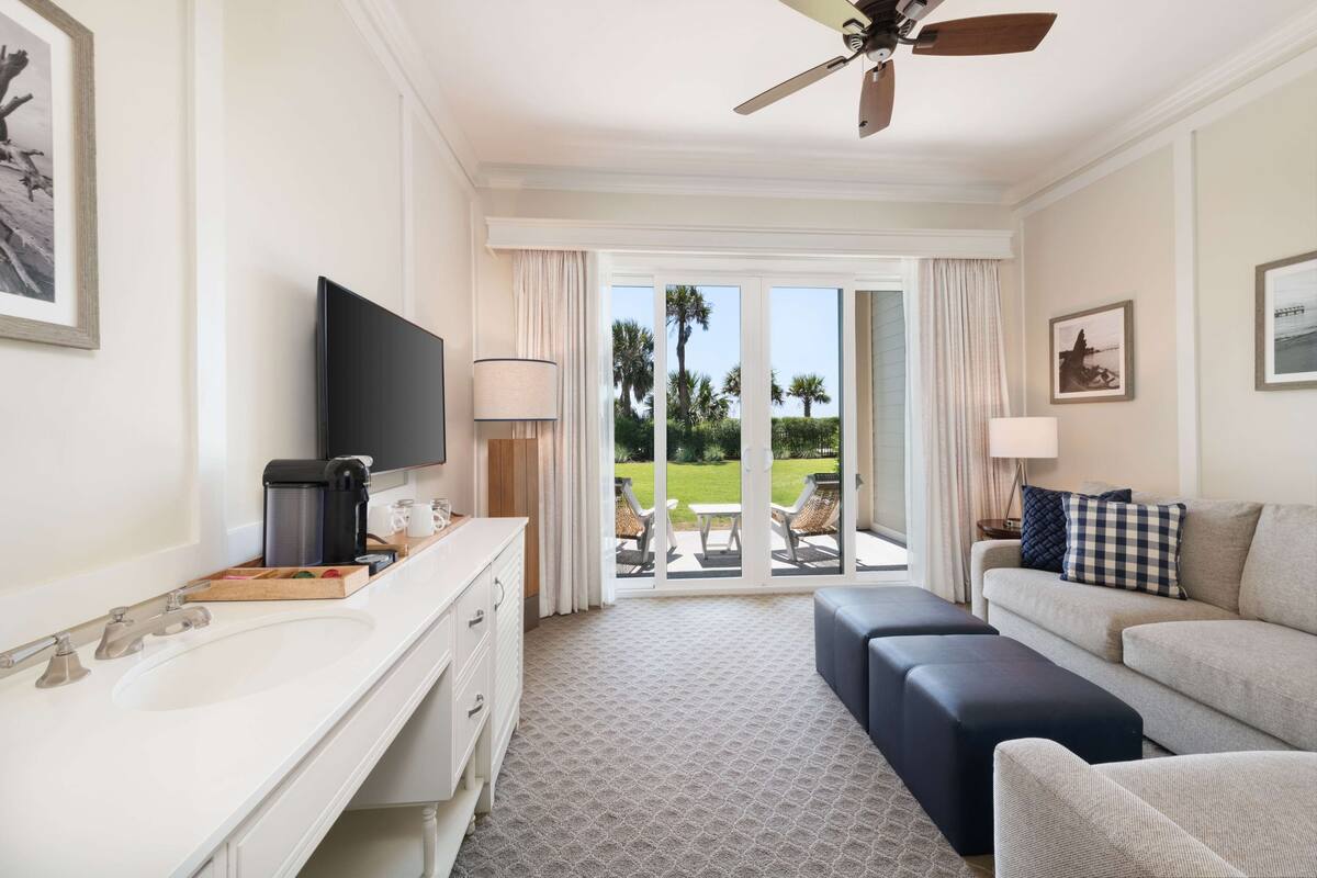 A hotel room with a large window, a flat-screen TV, a sofa, a coffee maker, and a lamp.