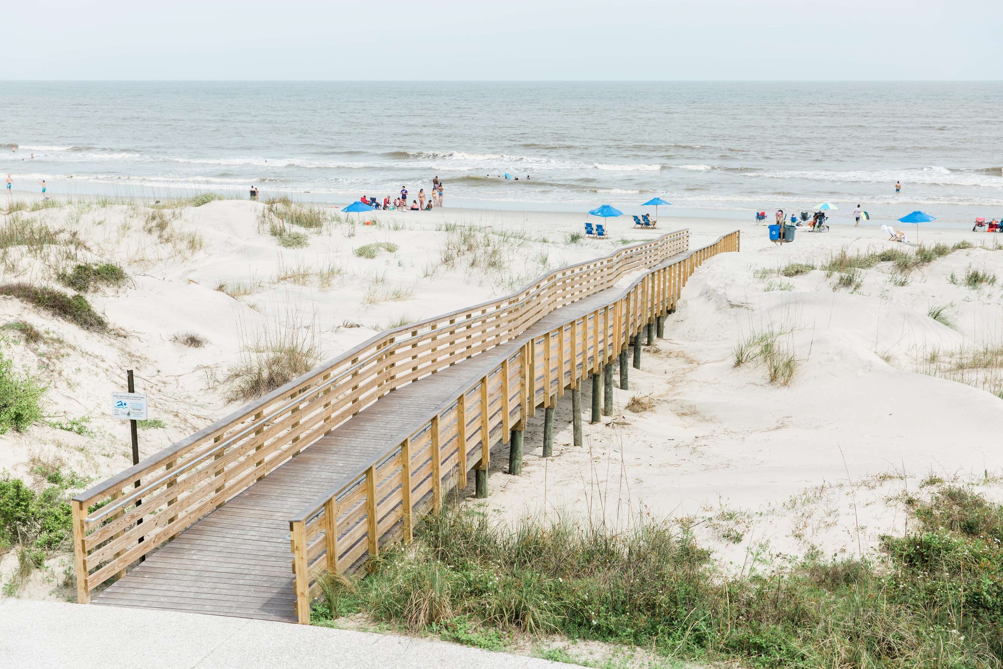 A wooden boardwalk leading to a beach with people and umbrellas.
