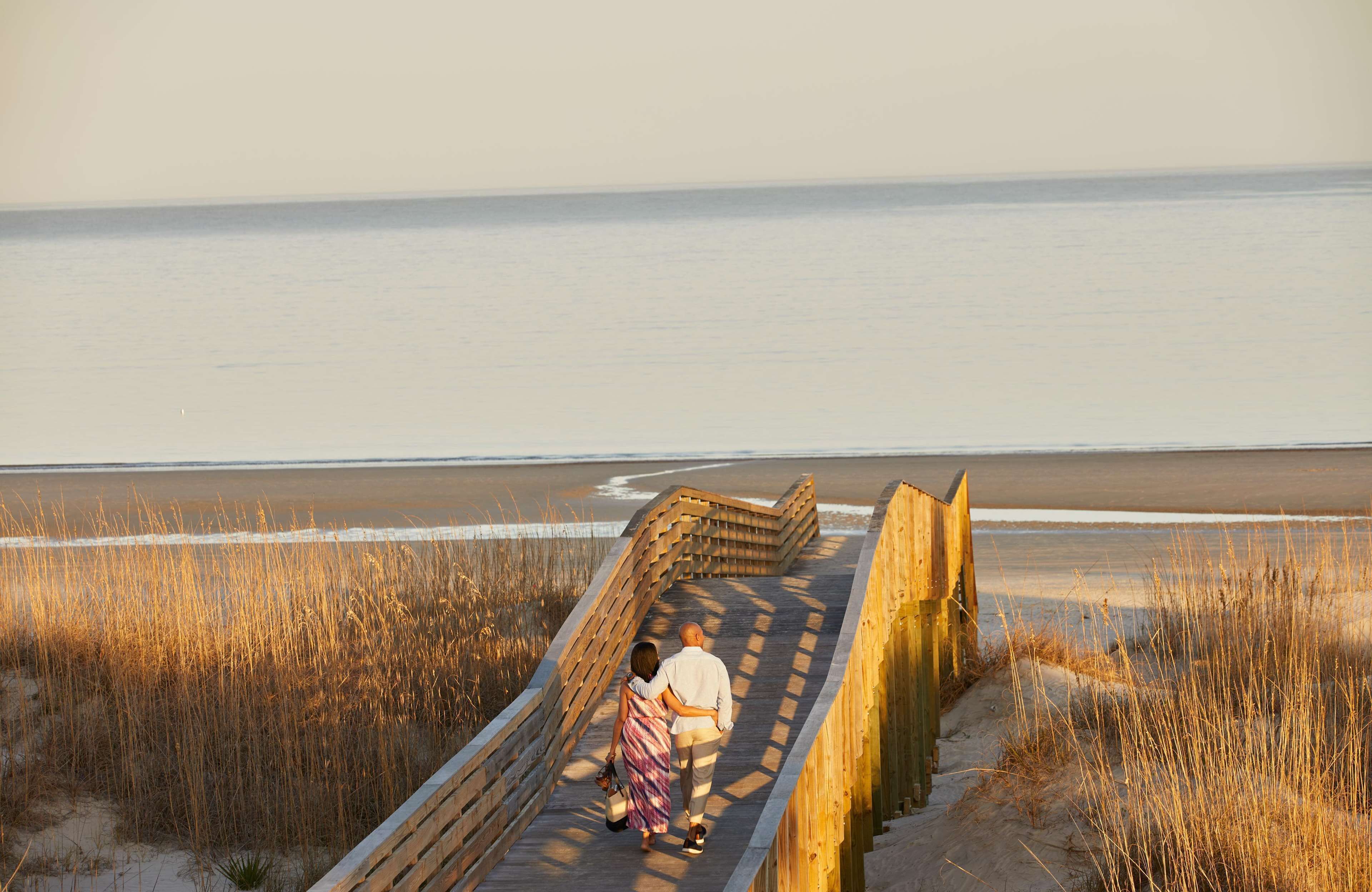 A wooden boardwalk leading to a beach with a calm sea in the background.