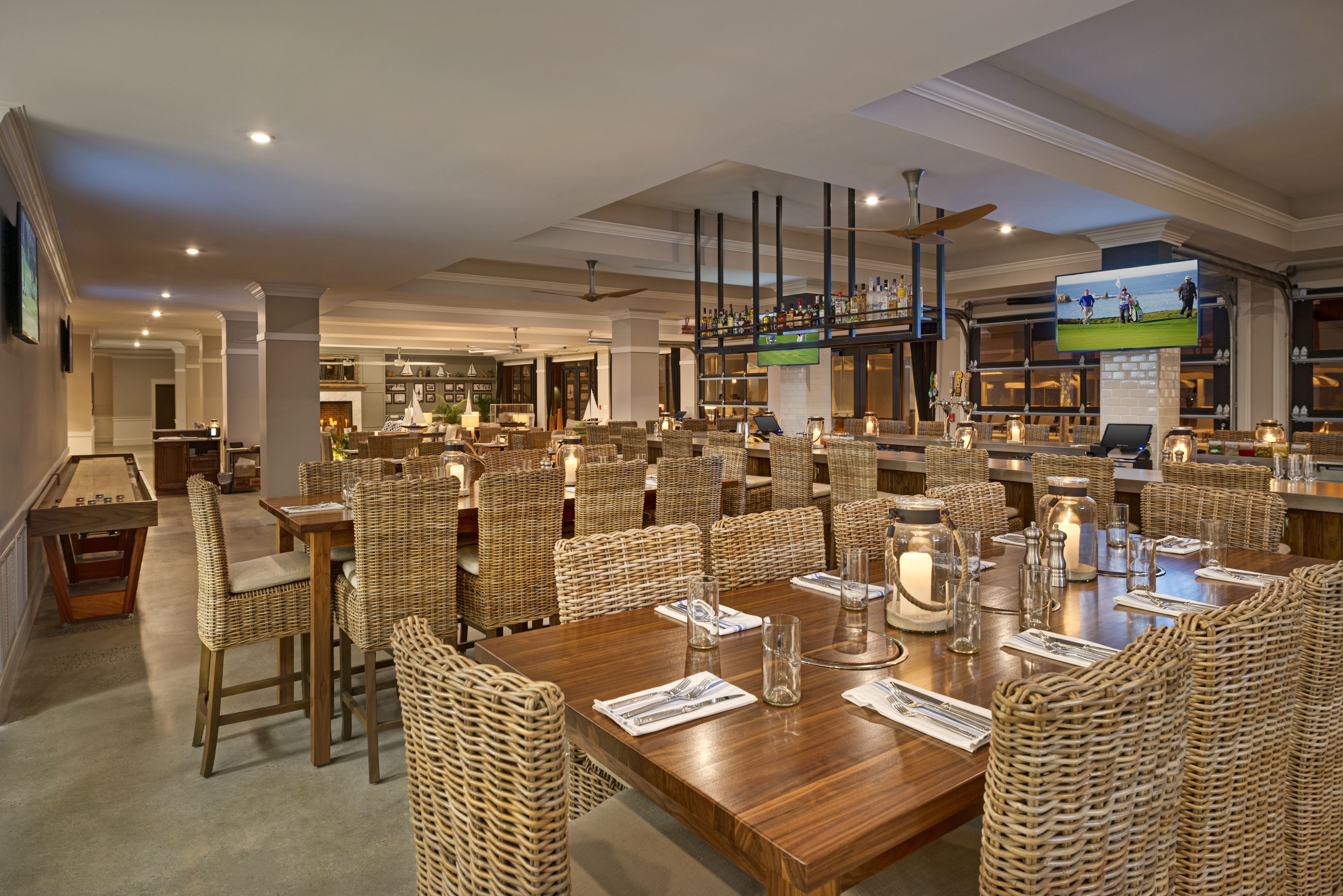 Un comedor amplio con mesas de madera altas y sillas de mimbre, una zona de bar con televisor y una mesa de billar.