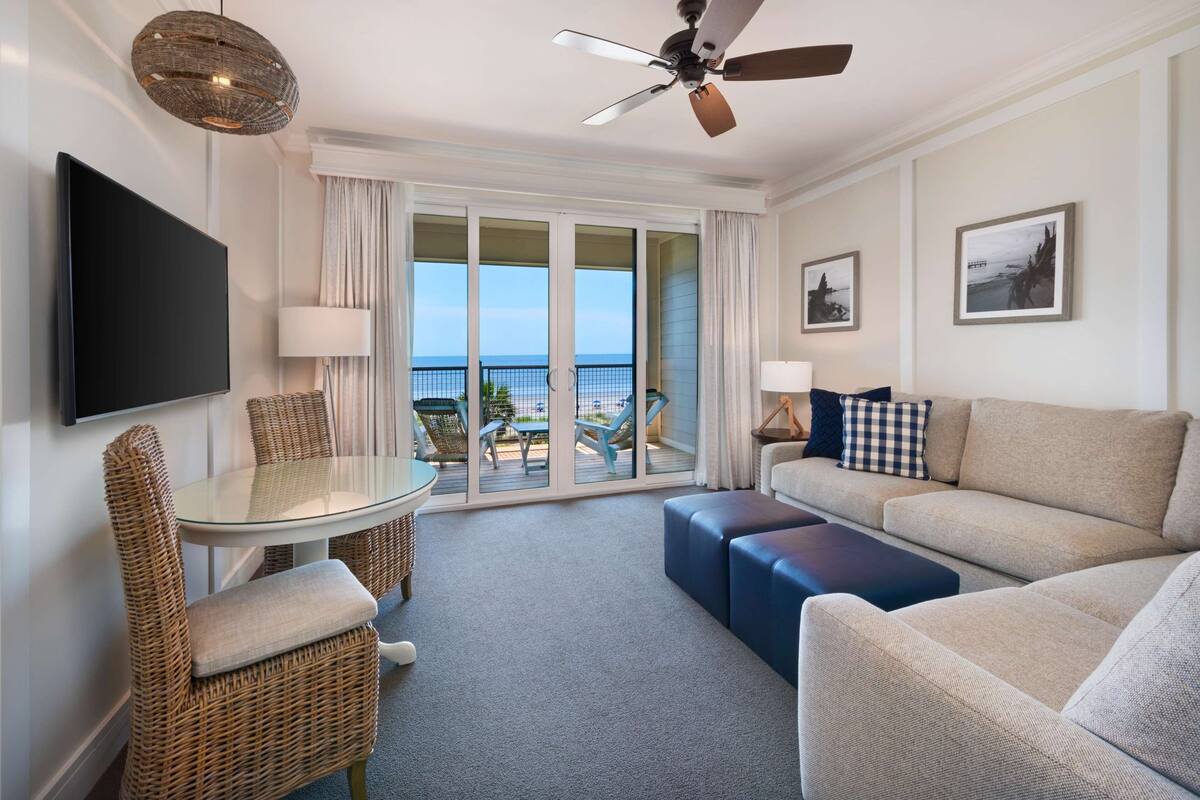 A hotel room with a balcony, a sofa, a table, and a TV.