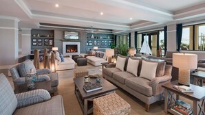 A spacious living room with a fireplace, comfortable seating, and large windows offering a view of the outdoors. - Jekyll Ocean Club (Jekyll Island)