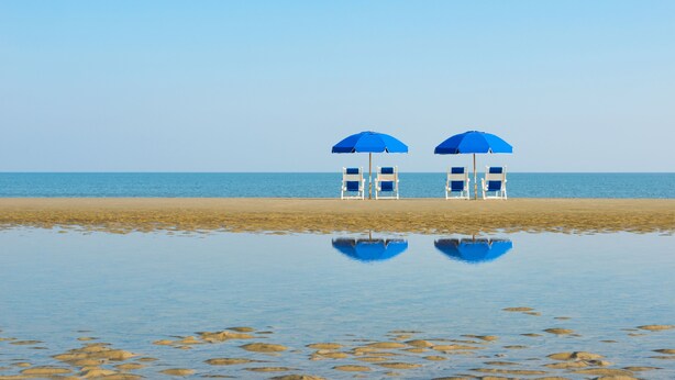 A beach with two blue umbrellas and white chairs. - Jekyll Ocean Club (Jekyll Island)