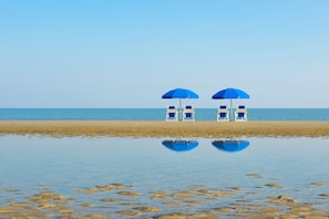 A beach with two blue umbrellas and white chairs. - Jekyll Ocean Club (Jekyll Island)