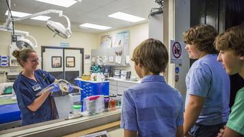 A medical professional in scrubs holding a fish in a laboratory setting with students observing.