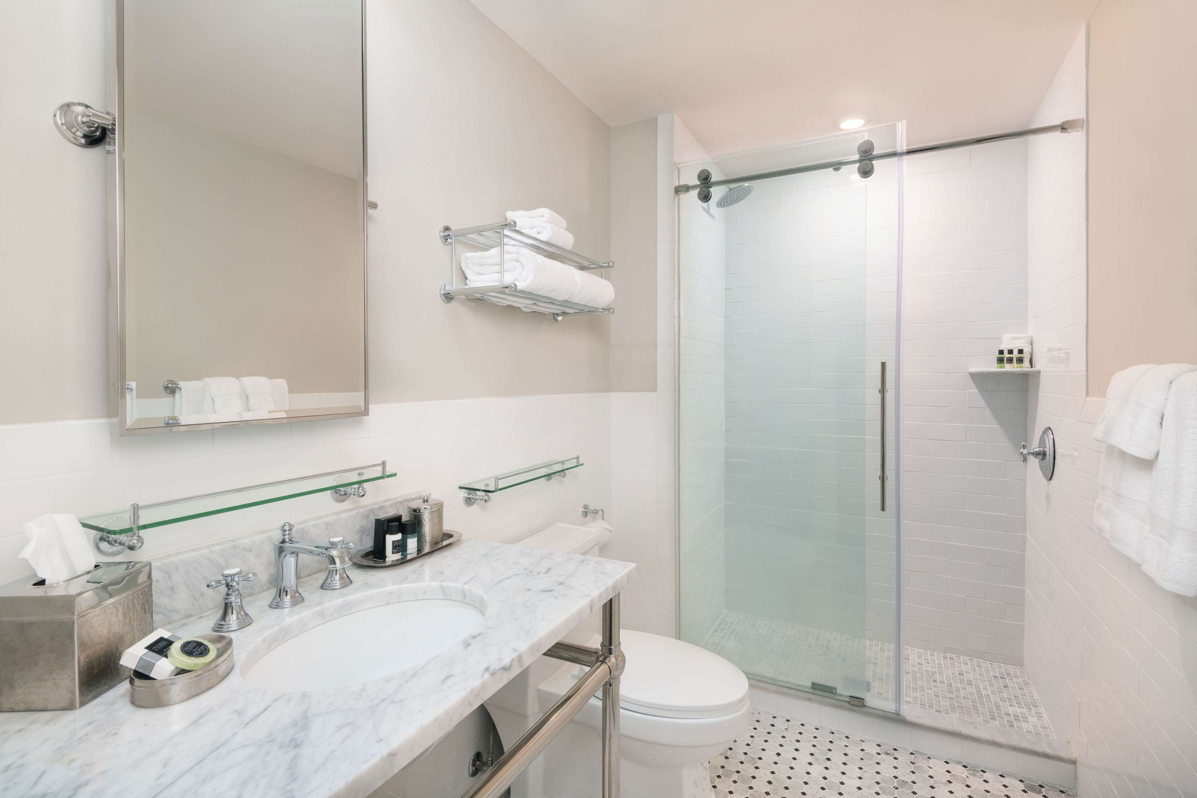 A modern bathroom with a marble sink, a large mirror, a glass shower enclosure, and neatly arranged towels.