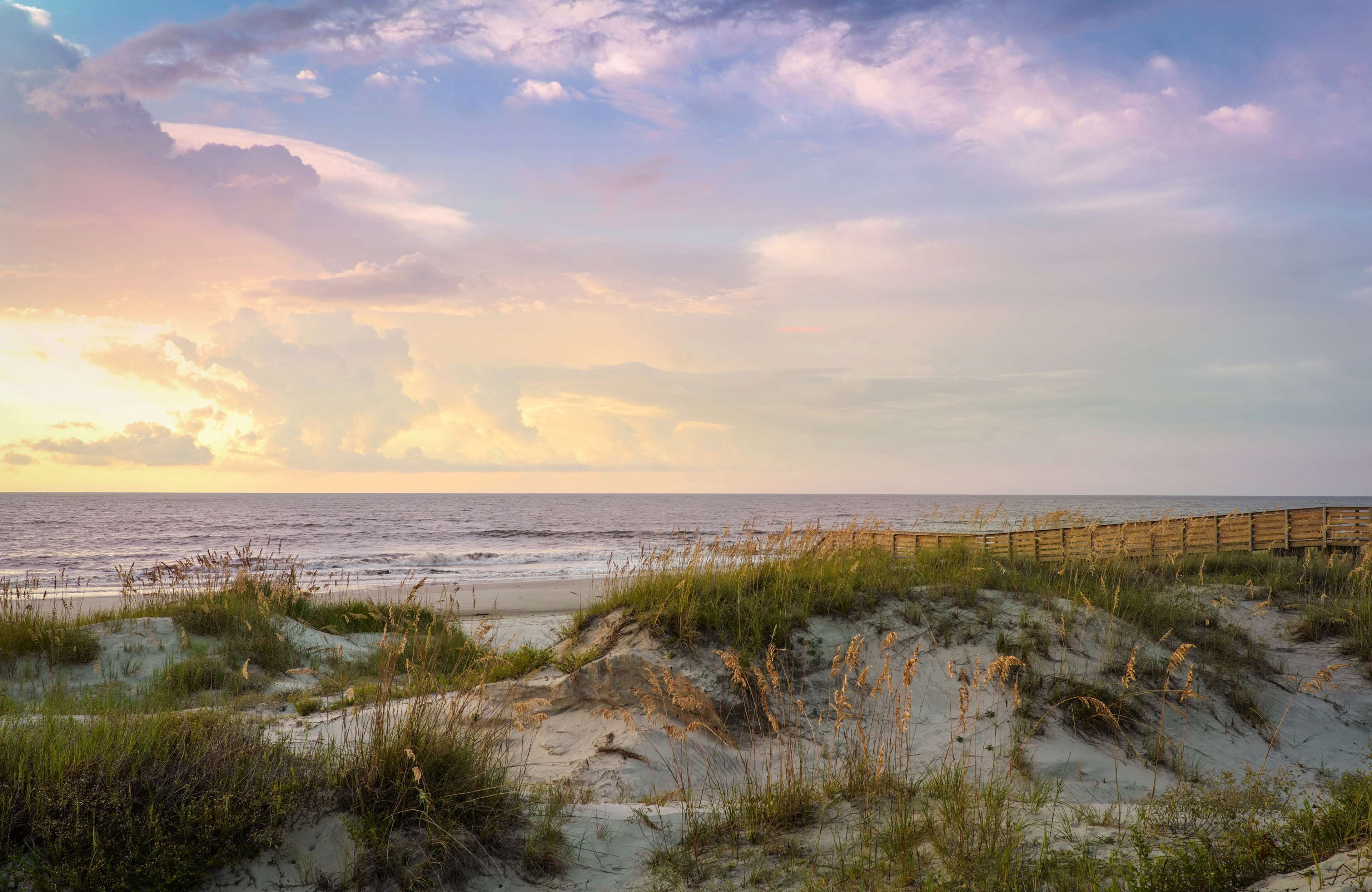 A beach with a wooden boardwalk, sand dunes, and the ocean.