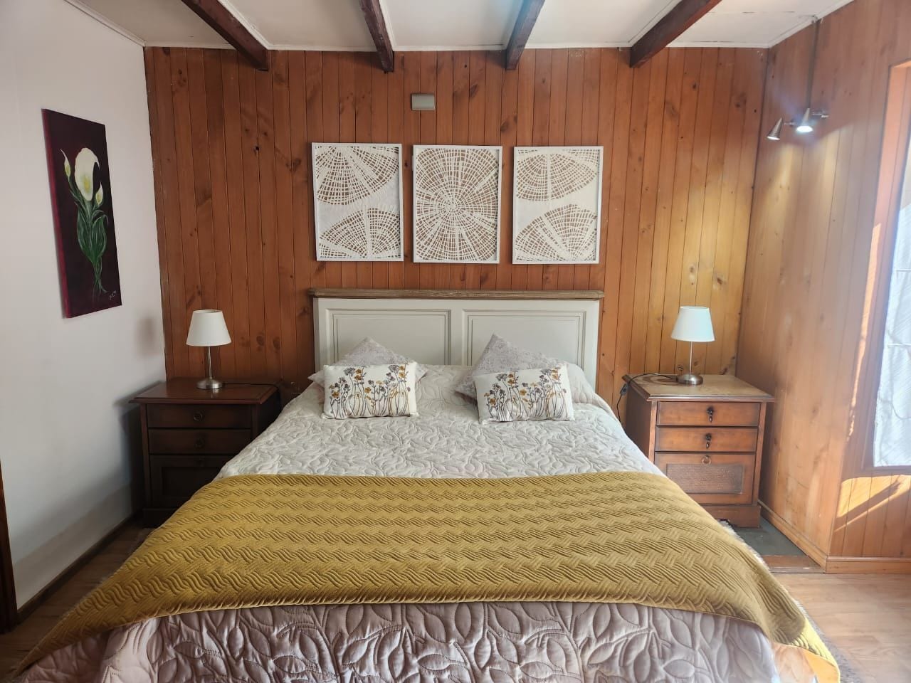 Une chambre à coucher comprenant un lit, deux tables de chevet, une lampe sur chacune, une grande fenêtre et un lambris en bois sur les murs.