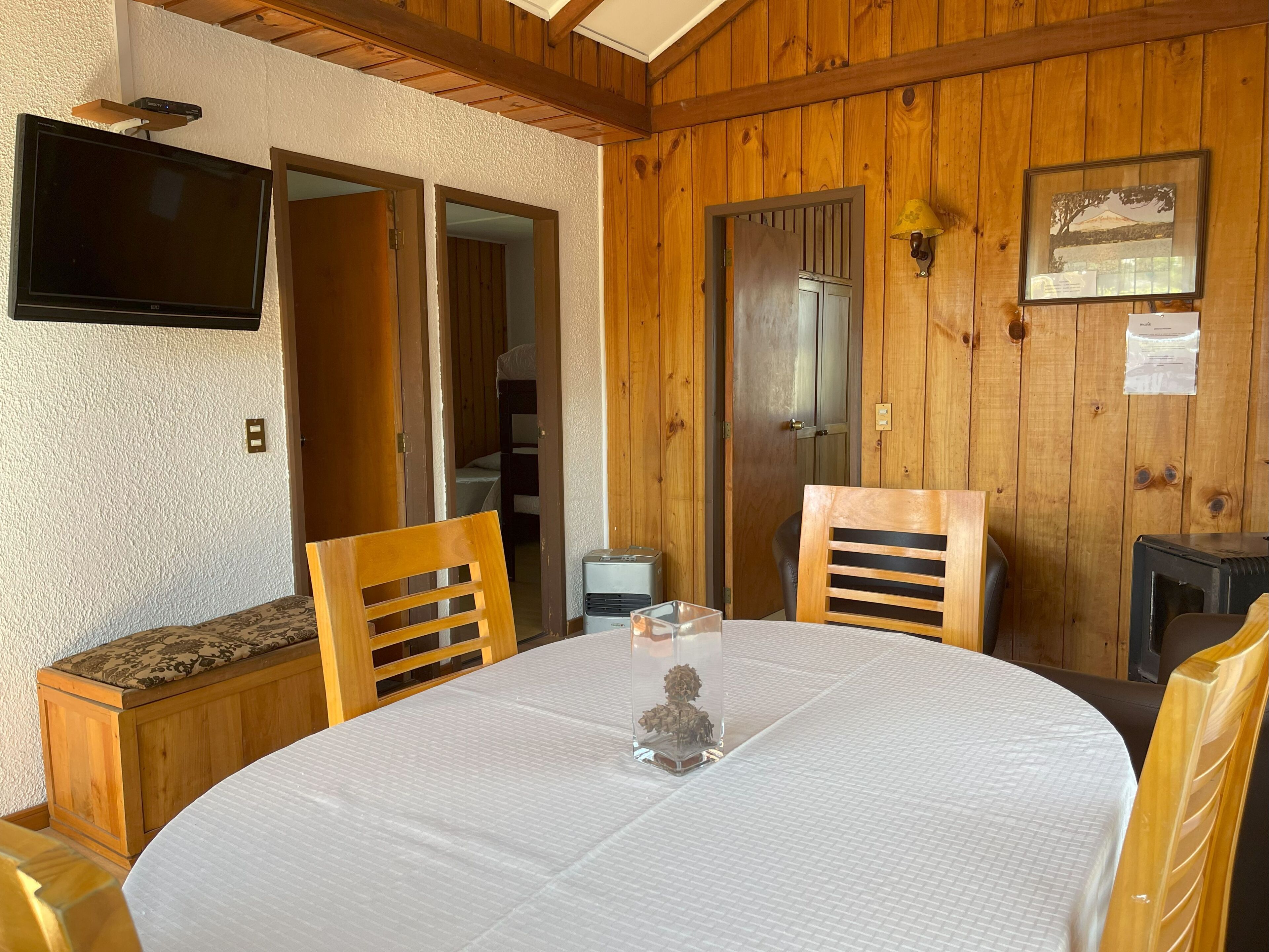 A wooden-paneled room with a round table, two chairs, a television on the wall, and a framed picture.