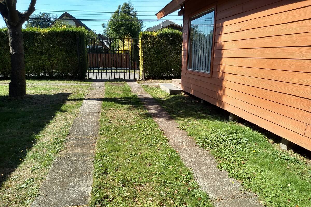 A pathway leading to a wooden house with a metal gate in the background.