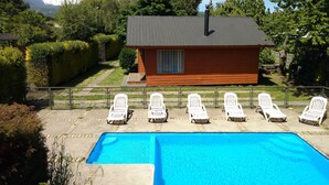 A wooden cabin with a swimming pool and white lounge chairs. - Cabañas Kernayel (Pucón)