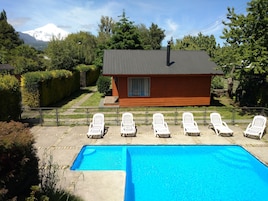 Una cabaña de madera con piscina y sillas de descanso blancas.