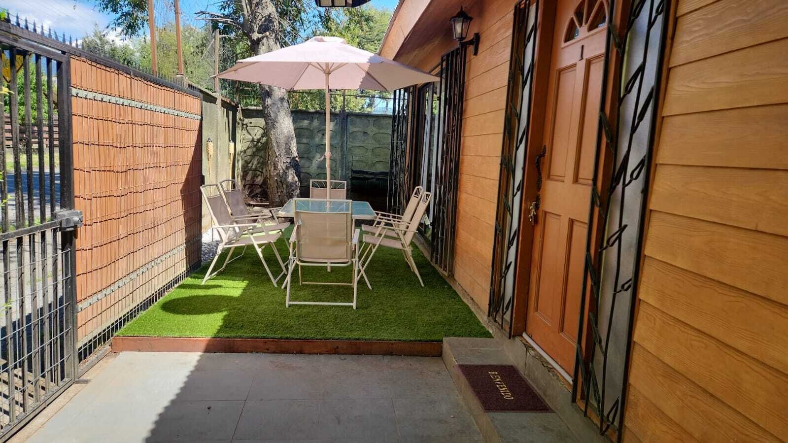 A patio with a table and chairs, a small lawn, and a wooden building with a door.