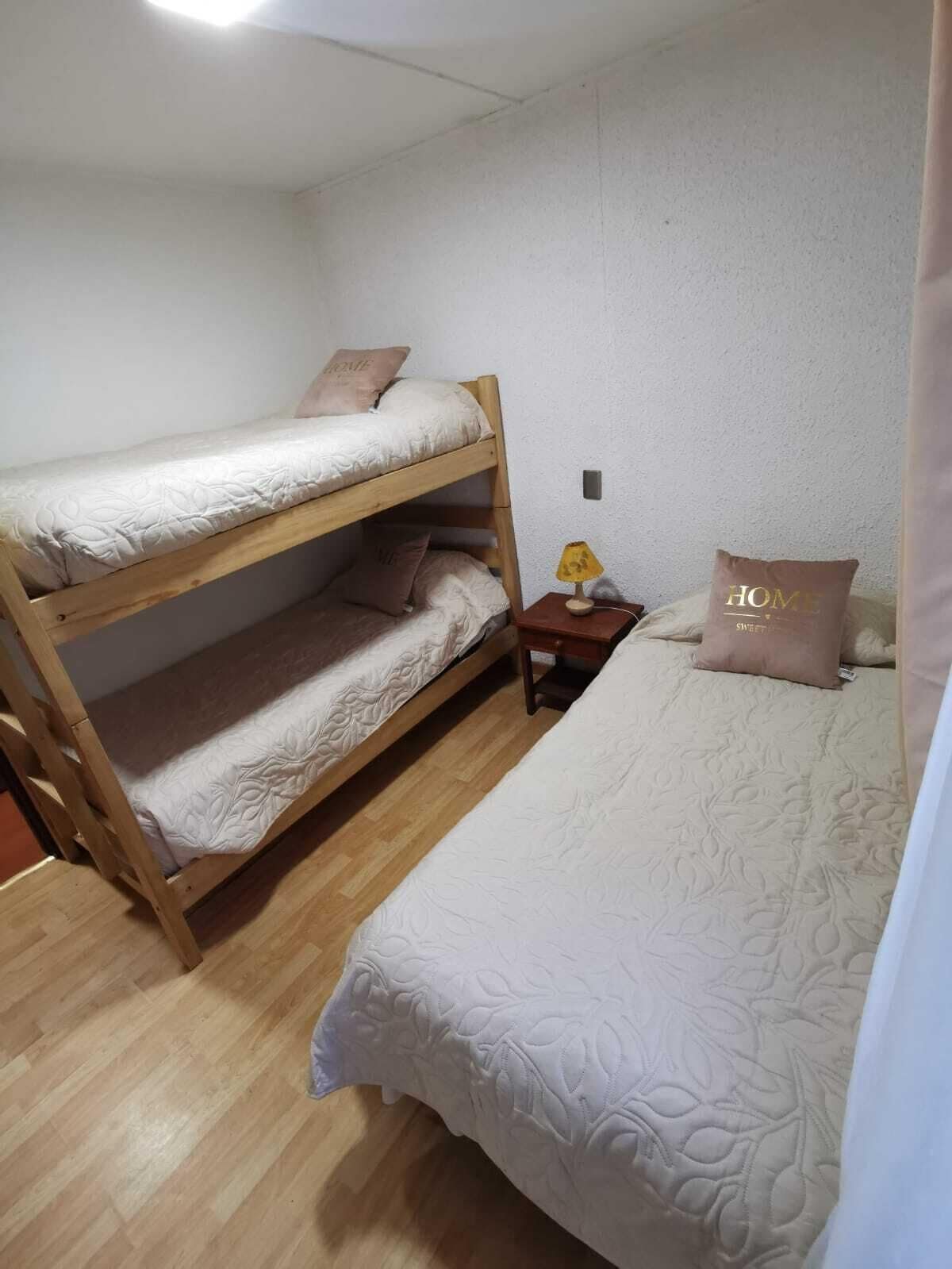 A bunk bed with two levels, a bedside table with a lamp, and a pillow with 'HOME SWEET HOME' text.