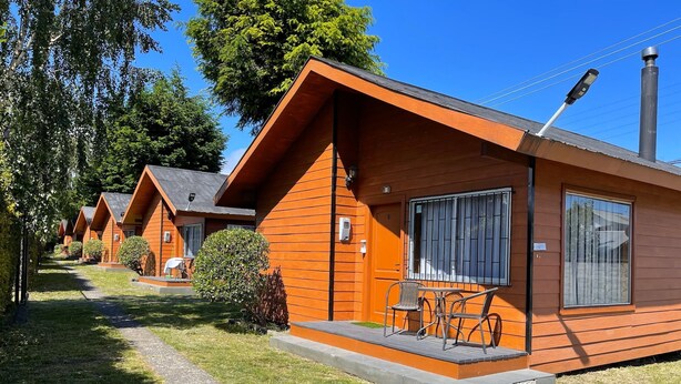 A row of wooden cabins with a small patio and a table with chairs. - Cabañas Kernayel (Pucón)