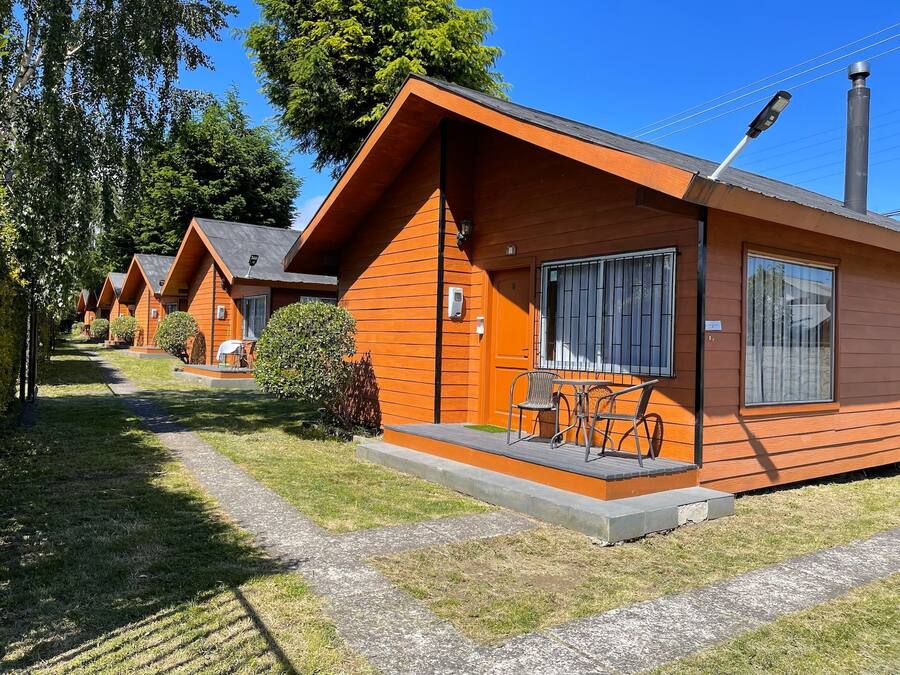 Una hilera de cabañas de madera con un pequeño patio y una mesa con sillas.