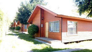 A row of wooden cabins with a sloped roof, a small porch, and a window with bars. - Cabañas Kernayel (Pucón)