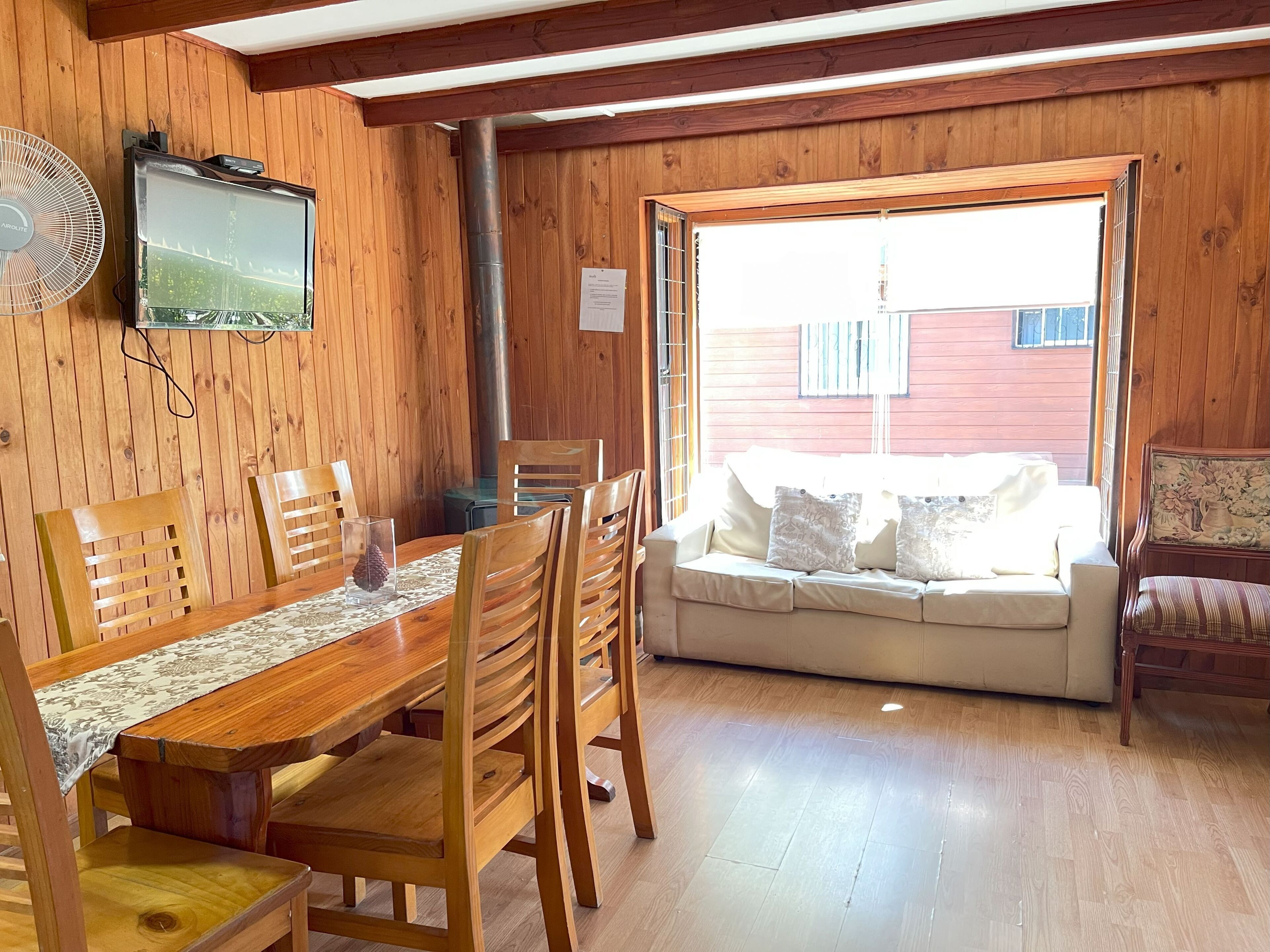 A wooden interior with a dining table, chairs, a sofa, and a television.