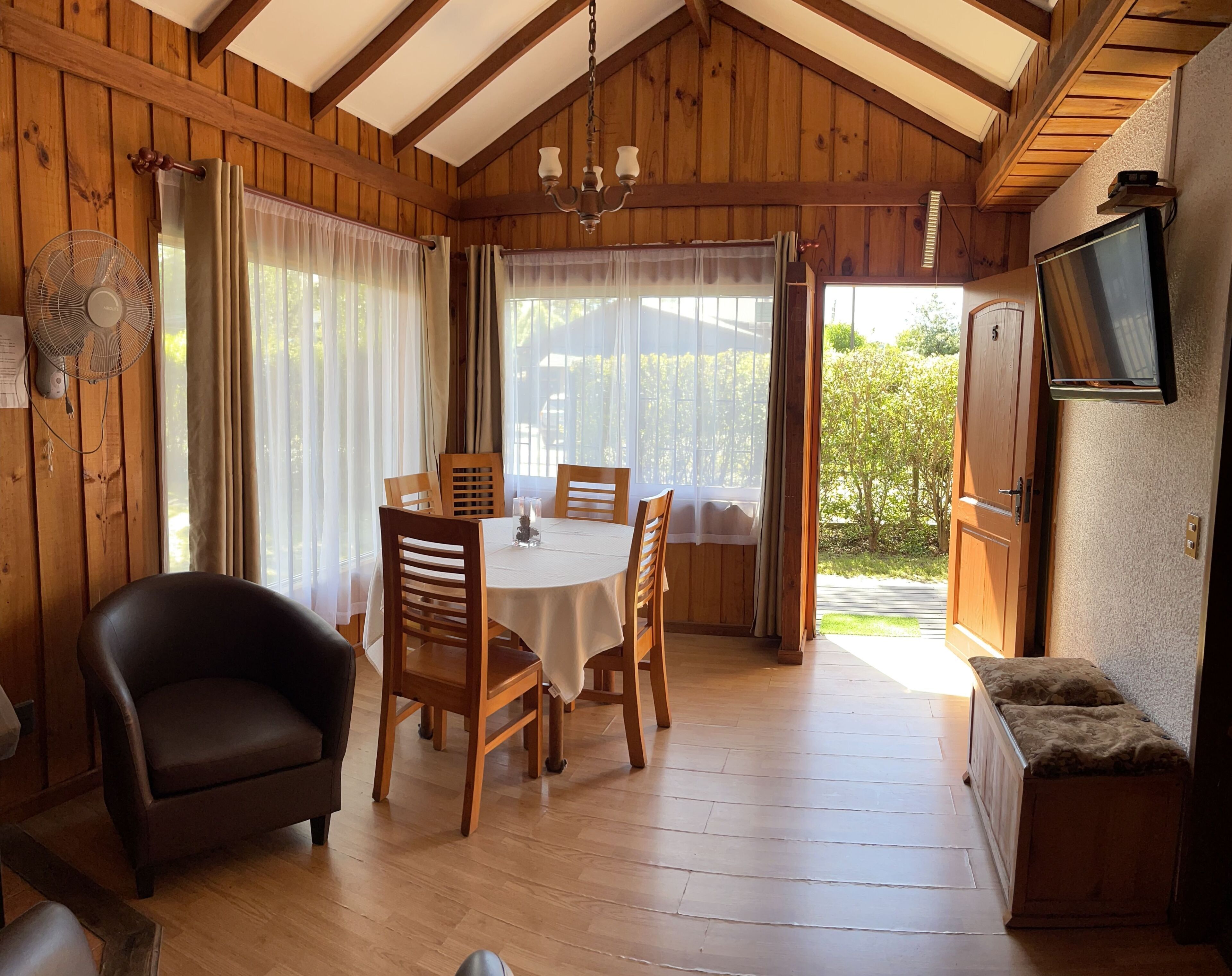 Un interno in legno con un tavolo da pranzo, sedie, un divano, una televisione e una ventola.