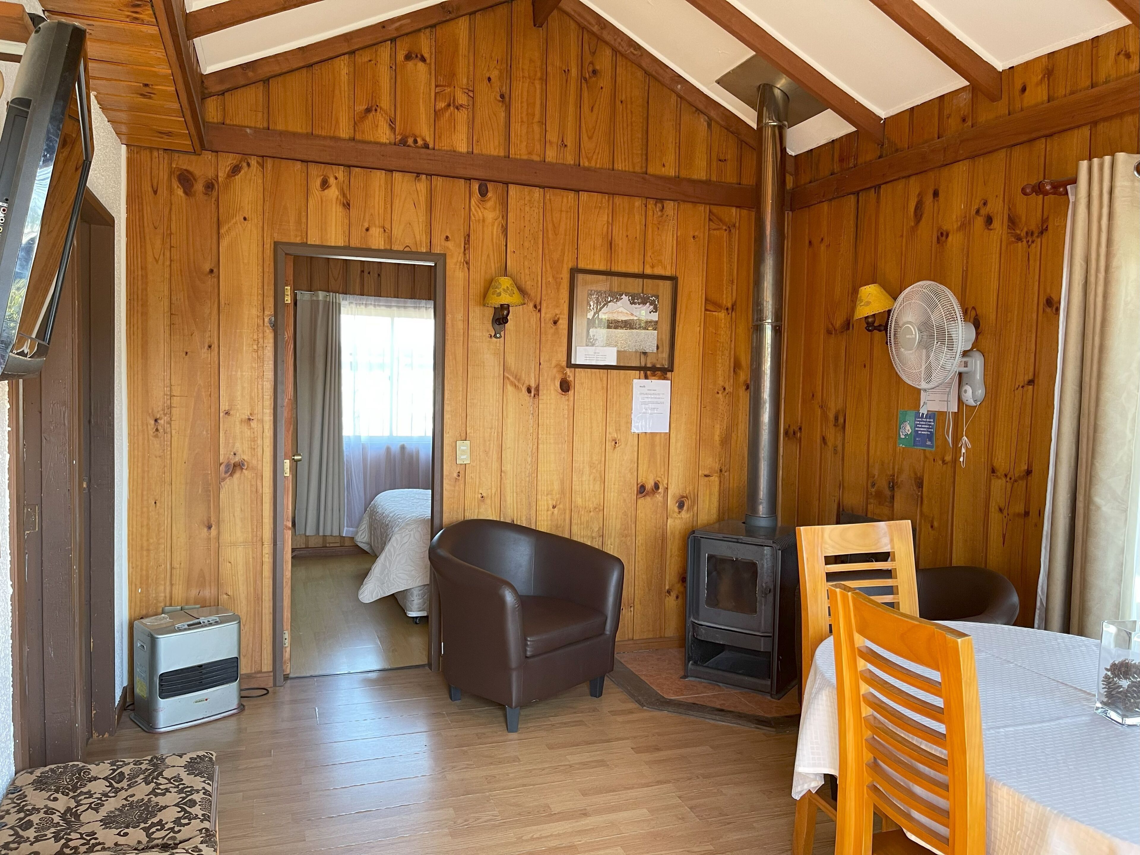 Interior de una cabaña con detalles de madera, un sofá, una mesa, un ventilador y un estufa de leña.