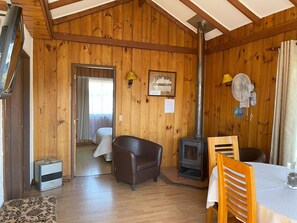 A cabin interior with a wooden interior, a sofa, a table, a fan, and a wood stove. - Cabañas Kernayel (Pucón)