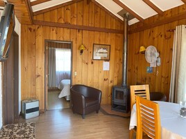 Interior de una cabaña con detalles de madera, un sofá, una mesa, un ventilador y un estufa de leña.