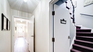 A hallway with a wooden floor, white walls, and a staircase with purple carpet. - Butterfly Manor Bed & Breakfast (Niagara Falls)