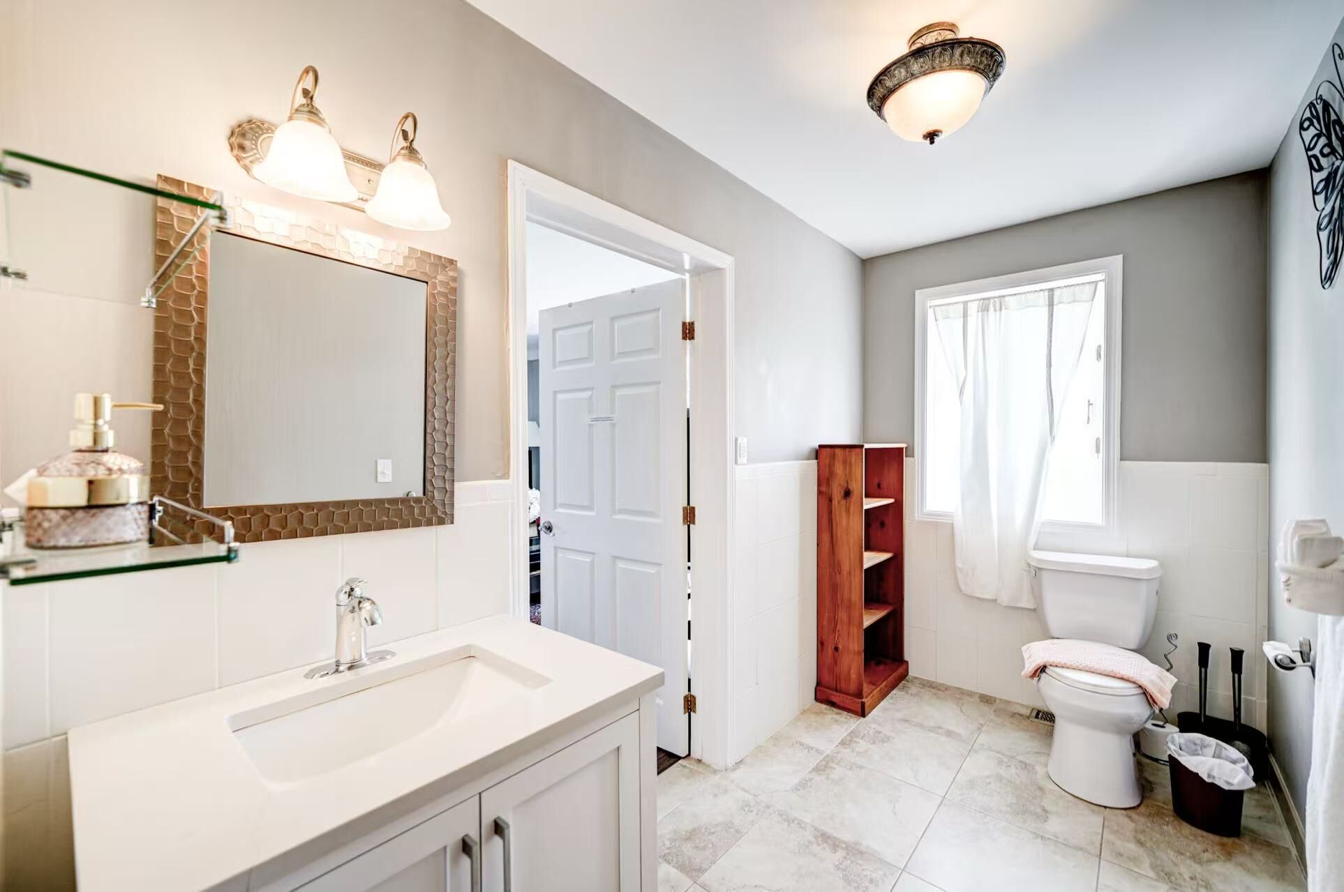 Een badkamer met een witte wastafel, spiegel en toilet. Er is een houten plankkast en een douchegordijn.