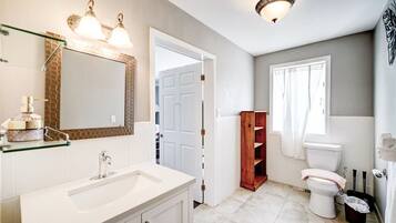 Een badkamer met een witte wastafel, spiegel en toilet. Er is een houten plankkast en een douchegordijn.