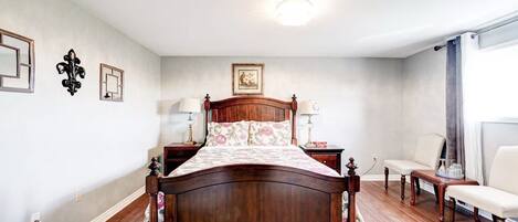 A bedroom with a wooden bed, two bedside tables, a chair, and a window with curtains.