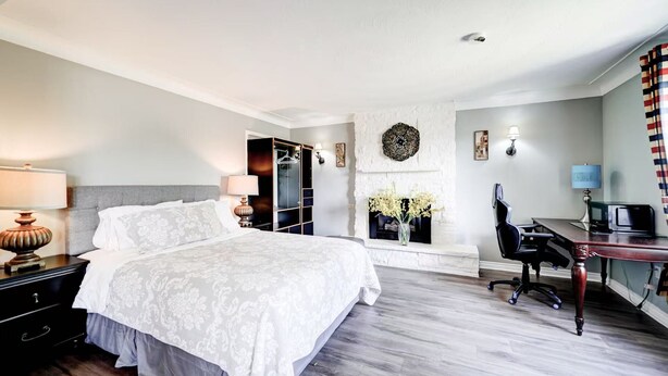A hotel room with a bed, desk, chair, lamp, wardrobe, and a fireplace. - Butterfly Manor Bed & Breakfast (Niagara Falls)