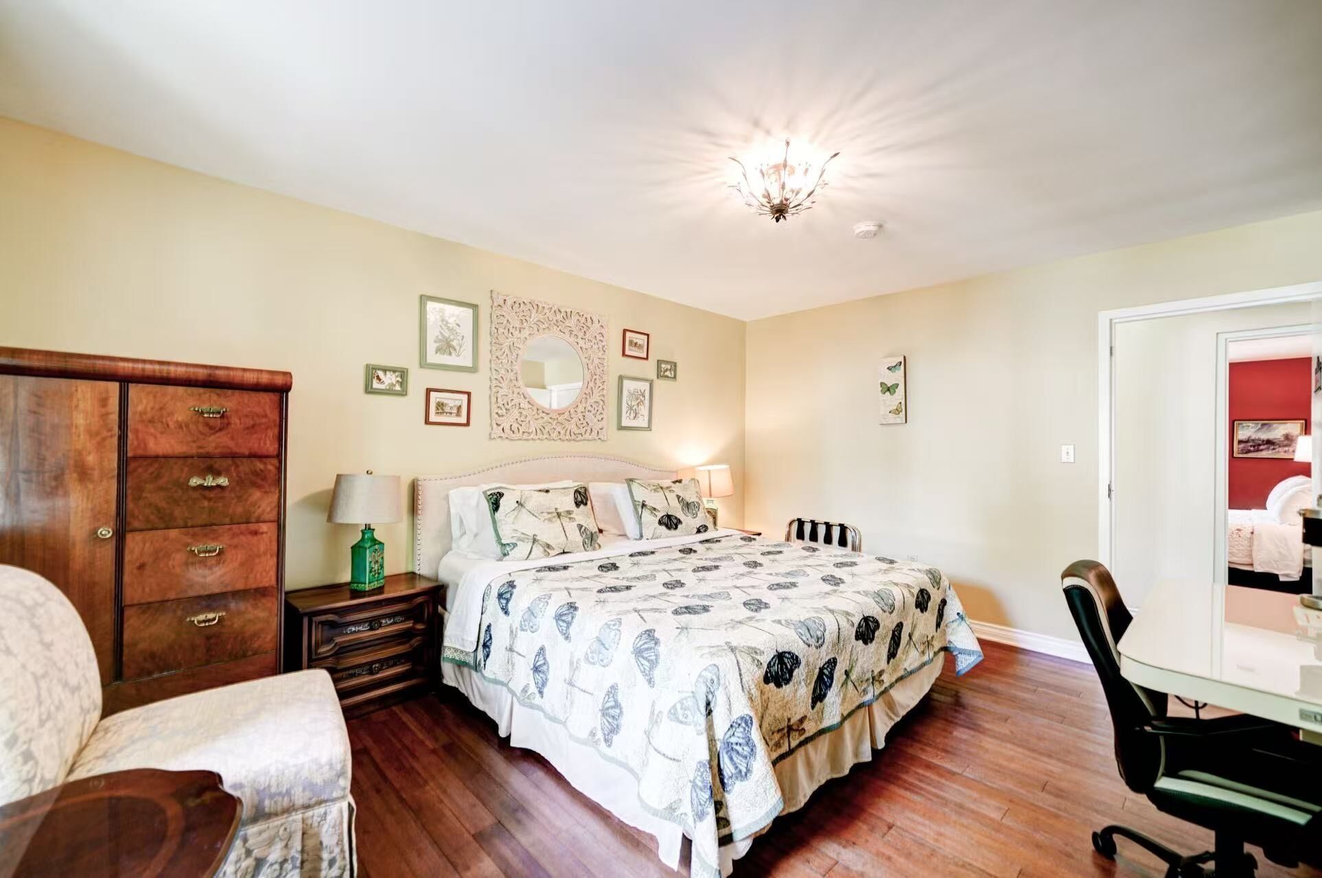 A bedroom with a bed, dresser, chair, desk, and a mirror on the wall.