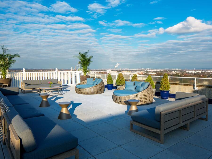 A rooftop terrace with outdoor seating, including sofas and chairs, and potted plants.