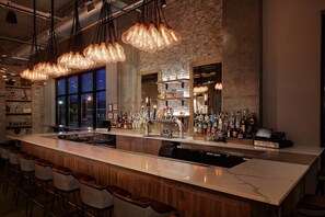 A bar area with a long counter, multiple stools, and a variety of bottles and glasses. - Watt Hotel Rahway, Tapestry Collection by Hilton (Rahway)