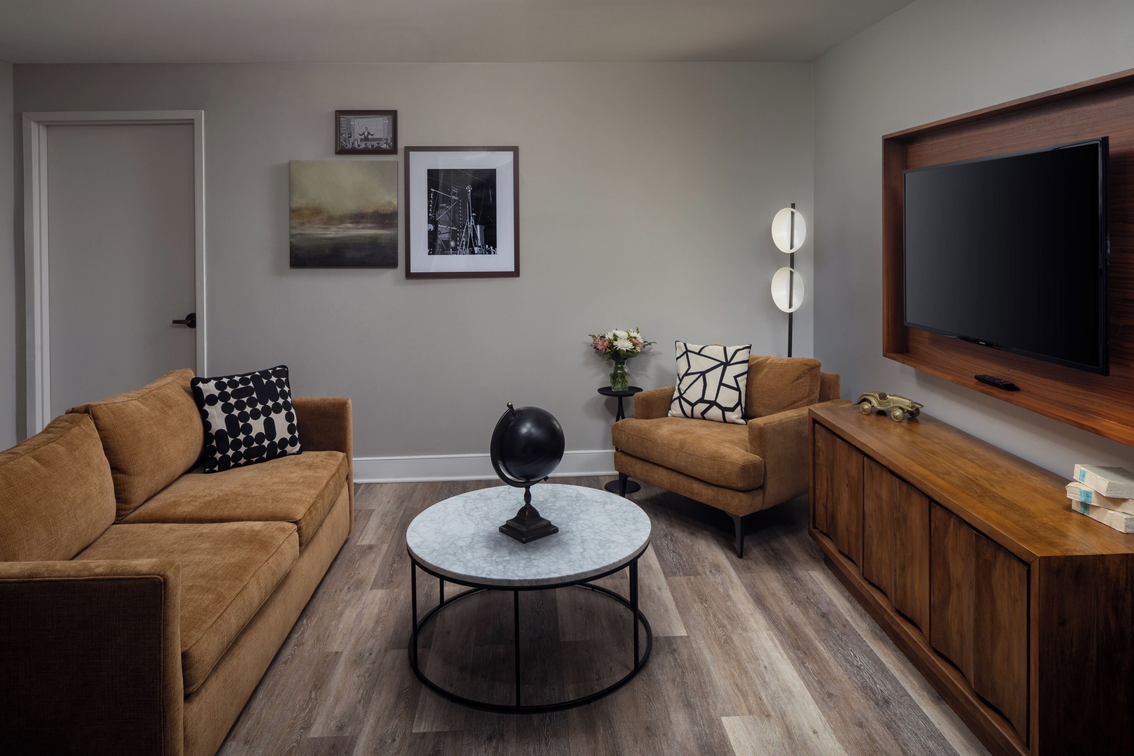 A living room with a sofa, armchair, coffee table, TV, and framed pictures on the wall.