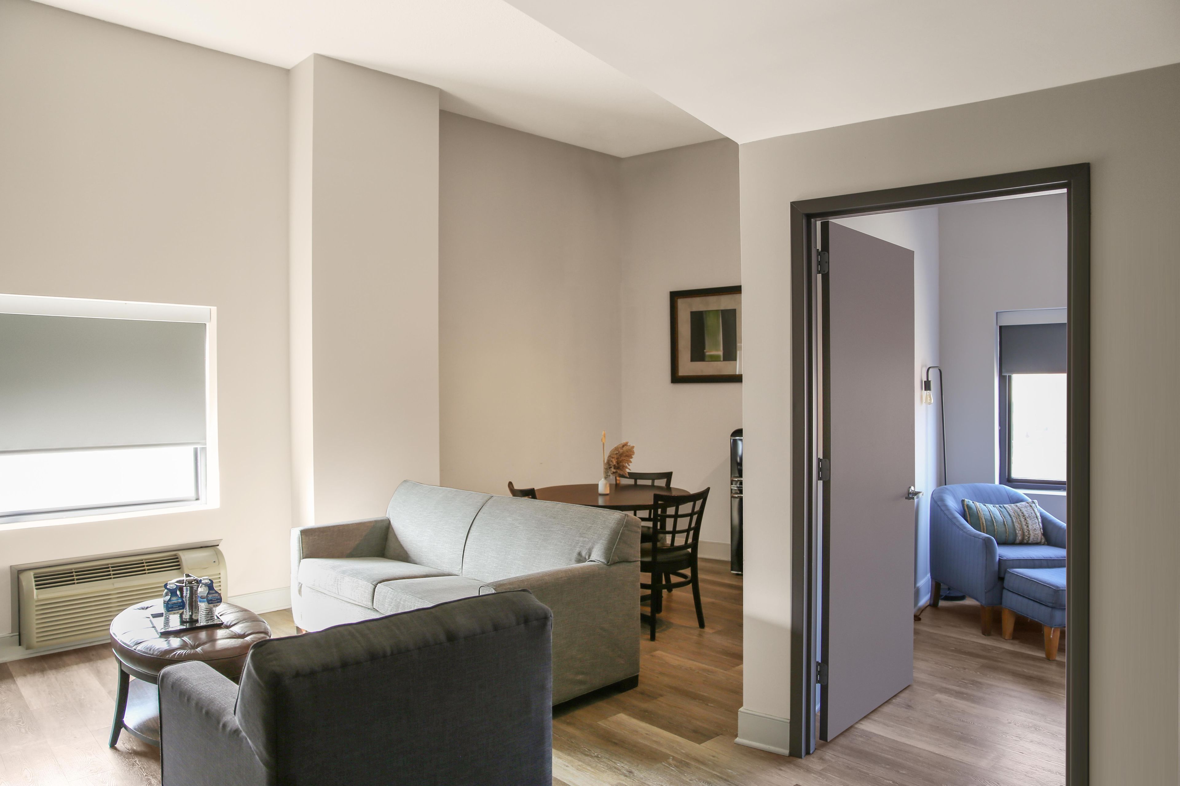 A living room with a sofa, a dining table with chairs, a television, and a door leading to another room.